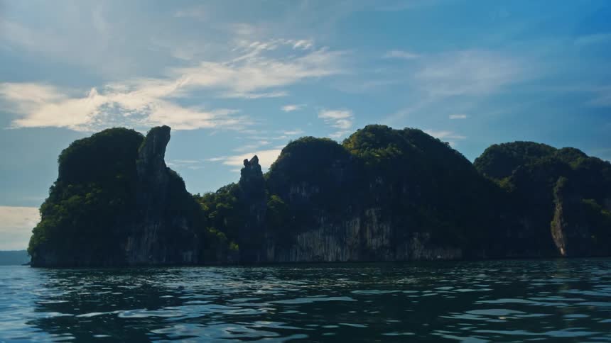 Lush rocky islands rising from the ocean under a partly cloudy blue sky