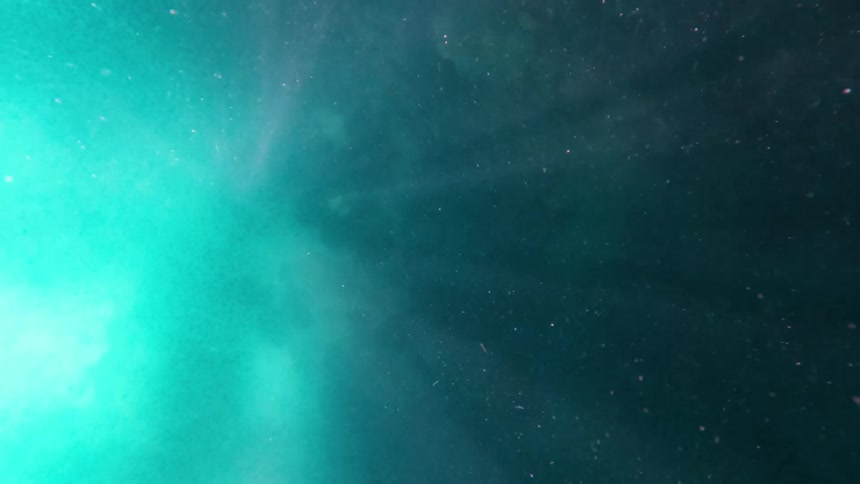An underwater gradient shifts from teal to deep blue with scattered light particles drifting above a murky ocean floor