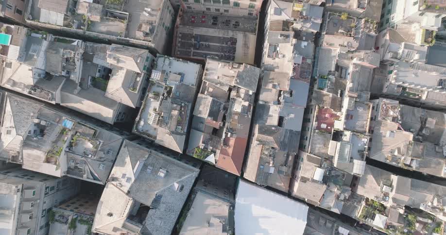 An aerial shot showcases a densely packed urban landscape with tightly knit buildings and narrow streets progressing towards a large structure with an inner courtyard
