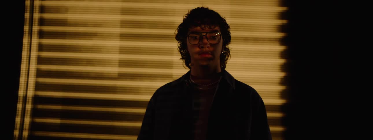 A young man in front of a large screen walking forward with a mysterious look