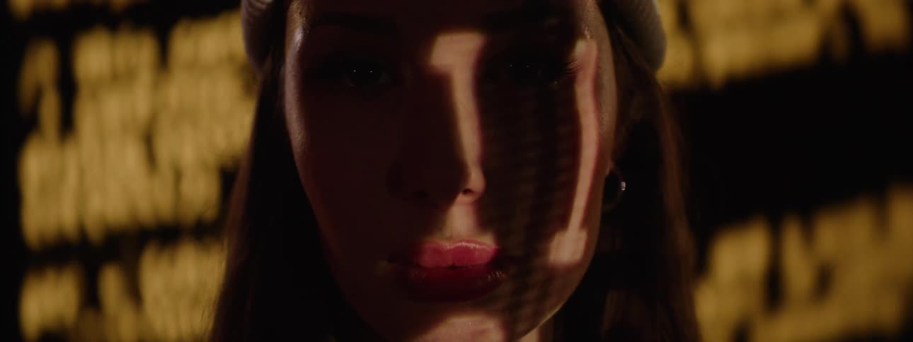 A woman in front of a large screen with numbers projected onto her face she opens her eyes and stares straight ahead