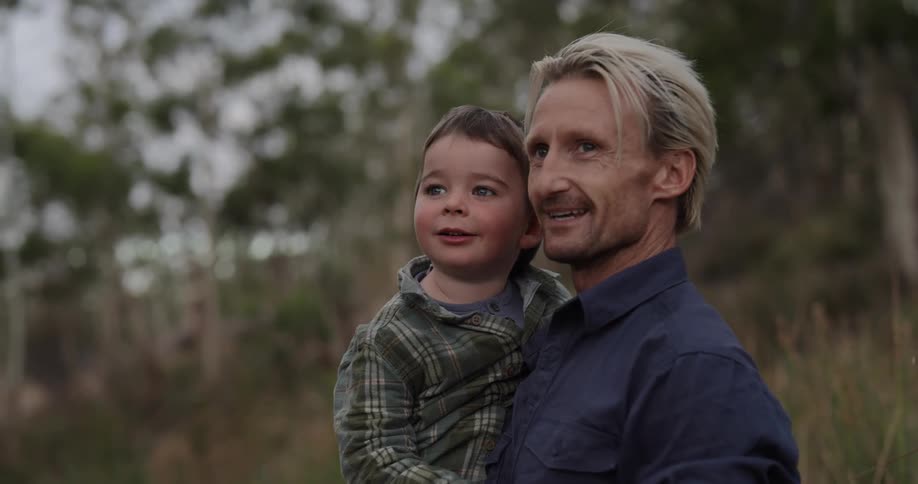 A father holding his young child in his arms looking at the horizon and pointing