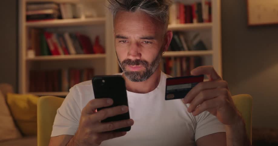 A man is using a credit card to pay for something on his cell phone