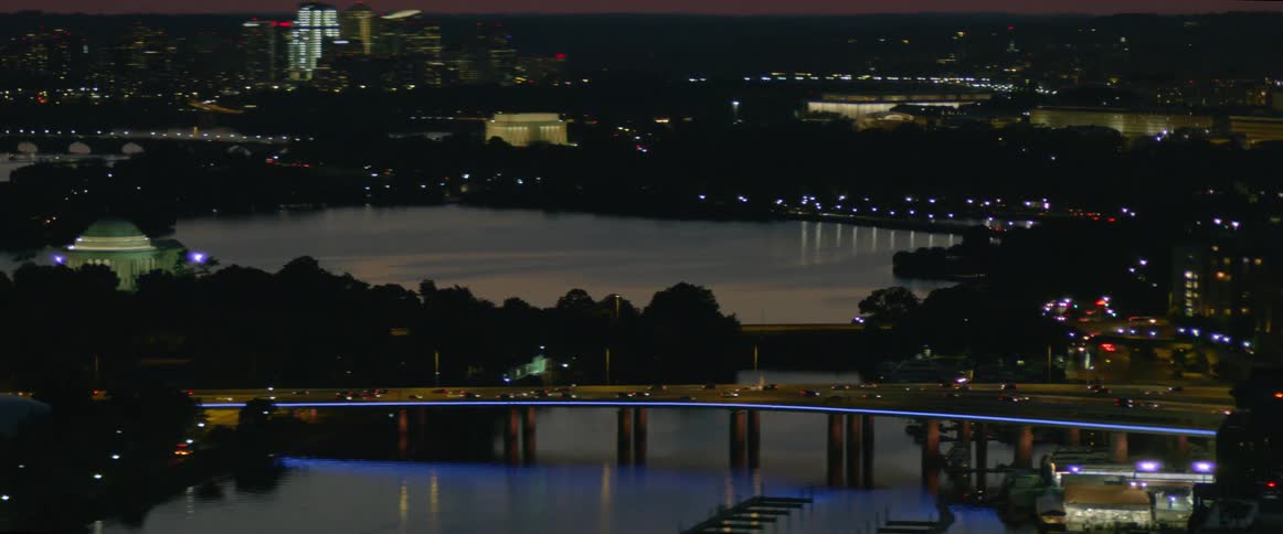 A bridge with traffic moving over a body of water by a large city at night