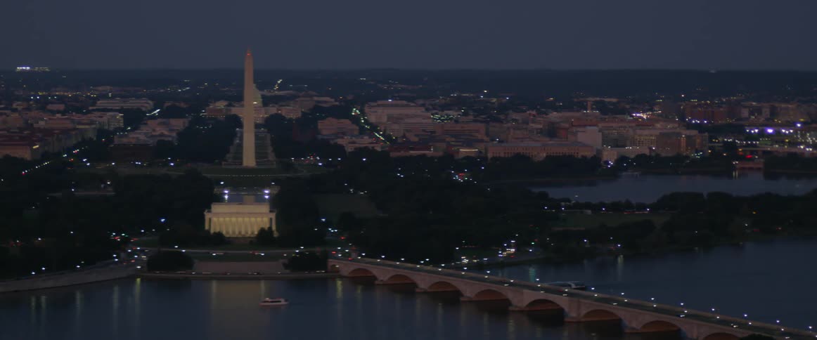 A bridge has lights along it leading to a city