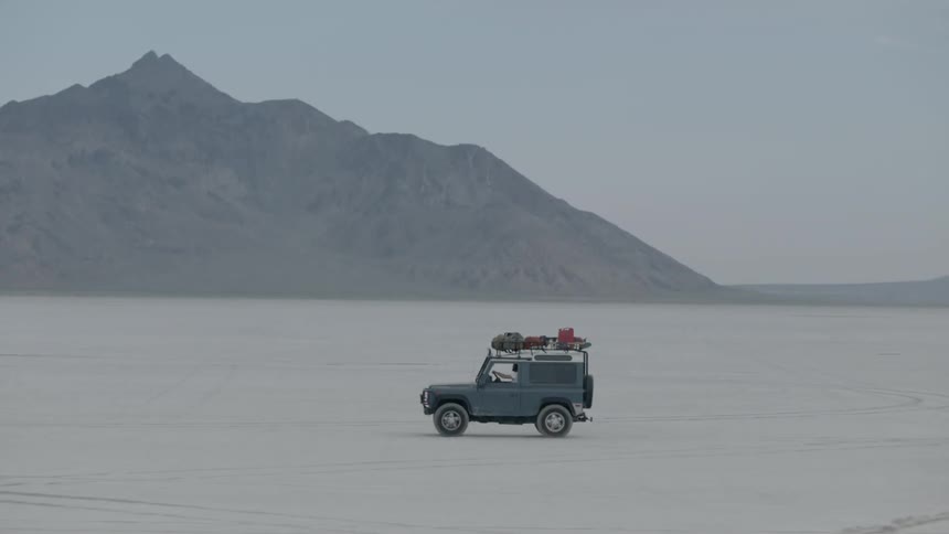 A blue jeep drives along a beach