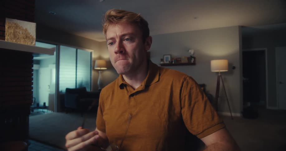 Blond man sitting down taking off his glasses and looking amazed