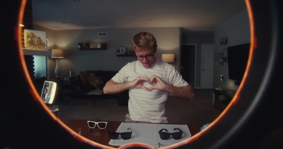 A man films himself through a ring light while sending playful flying kisses and expressing affection