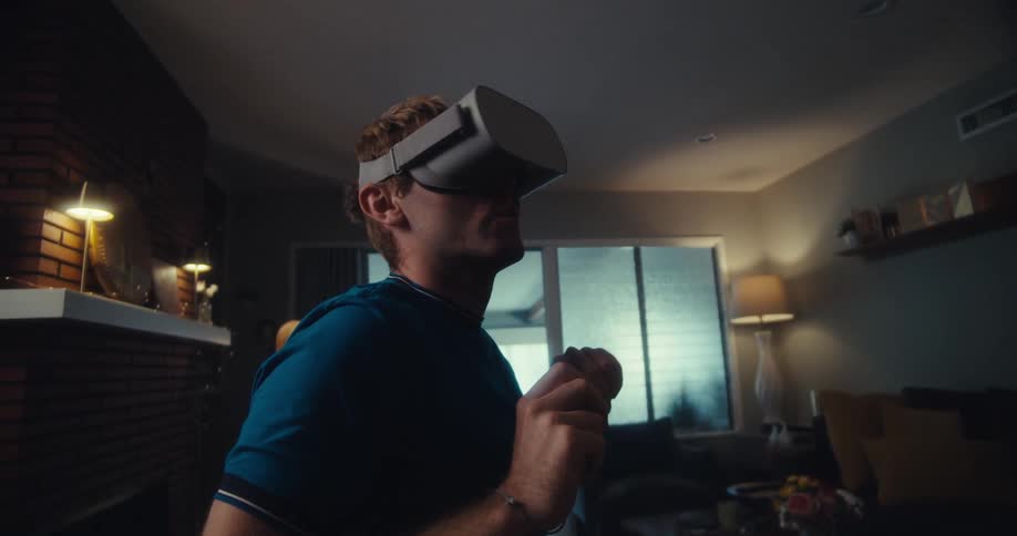 A man wearing a vr headset is playing an exciting game in his living room slowly turning his head left and right in fear