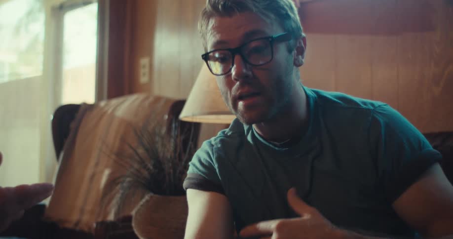 Man sitting on a sofa gently touches the face of a man wearing a cap during a conversation in a cozy living room