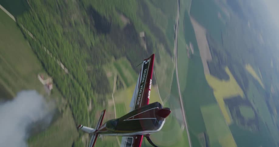 An acrobatic plane performs a vertical climb with smoke trailing behind over a rural landscape