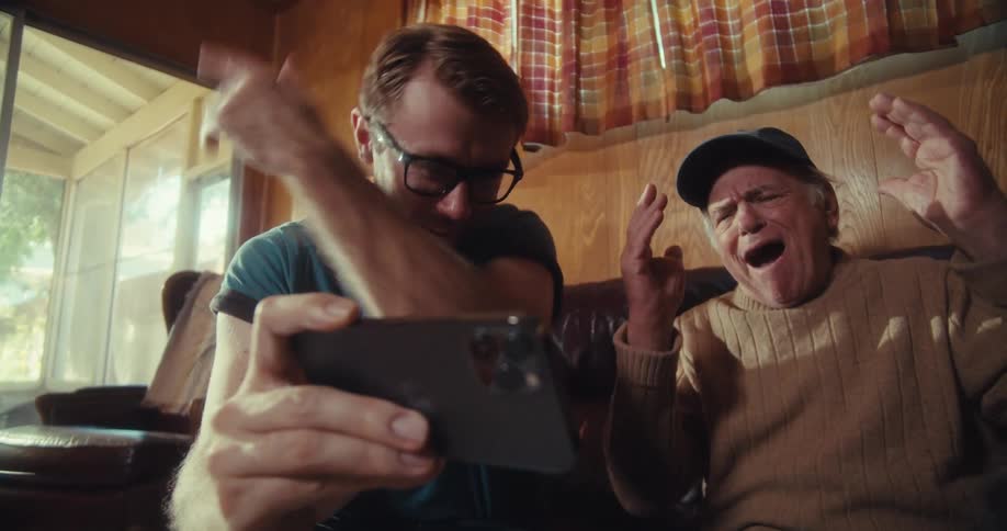 Two men throw their hands up while looking at a cell phone