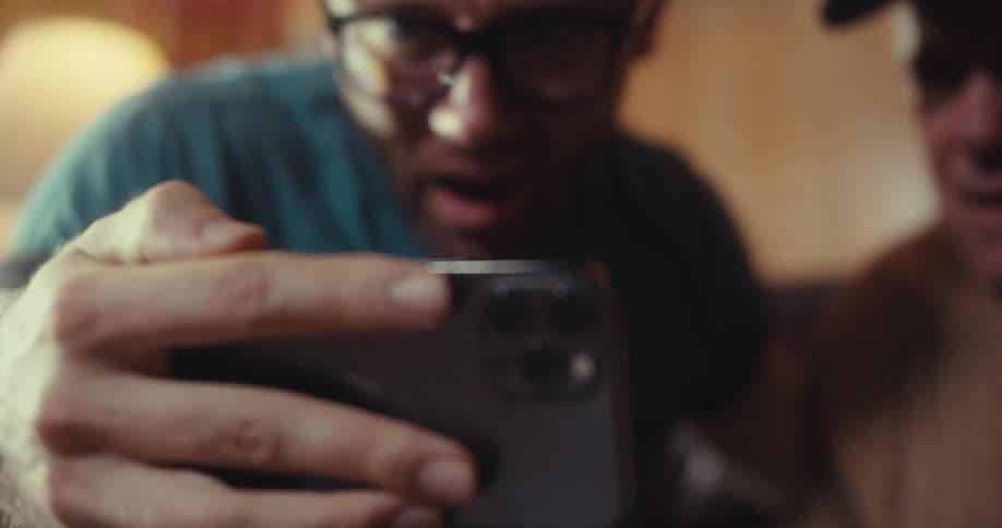 Two men are closely watching a cell phone screen