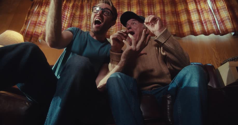 Two men cheer while watching a cell phone on the couch