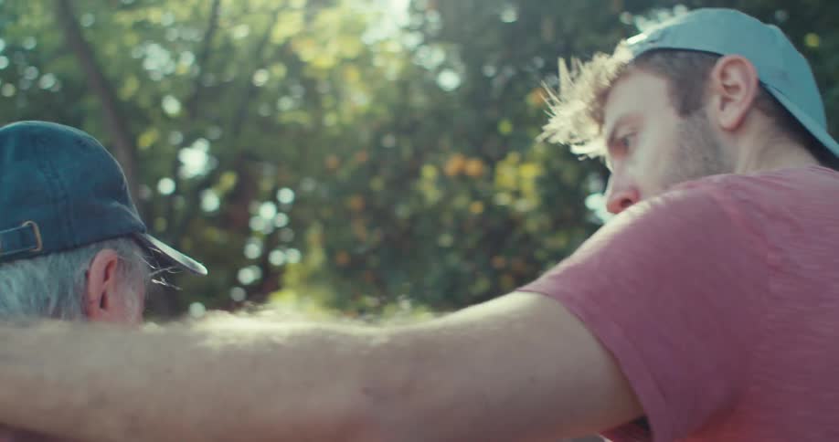A young man is hugging an elderly man and they are walking forward while talking