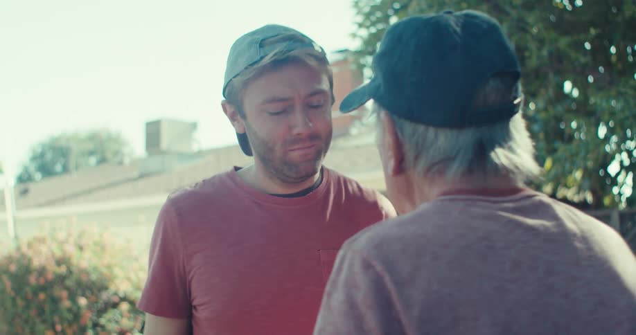 Two men embrace outdoors in an affectionate moment under the sunlight