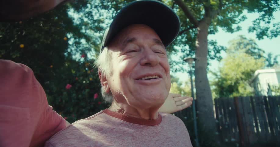 Elderly man and his grandson laugh while standing in the backyard and talking