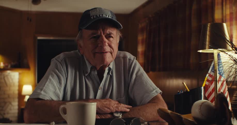 An elderly man sits at a desk writes something and thinks