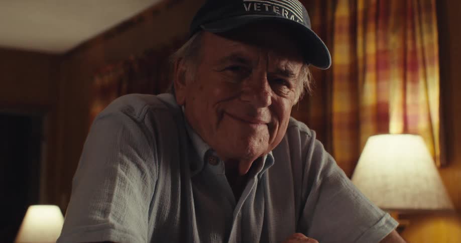 Man in a hat smiles and sits at a counter in his home