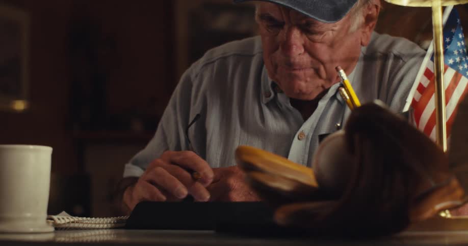 Elderly man consulting a device while writing in a notebook becomes upset