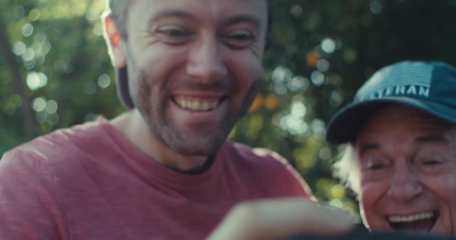 Two men react with surprise and excitement after seeing something on a cell phone while outdoors