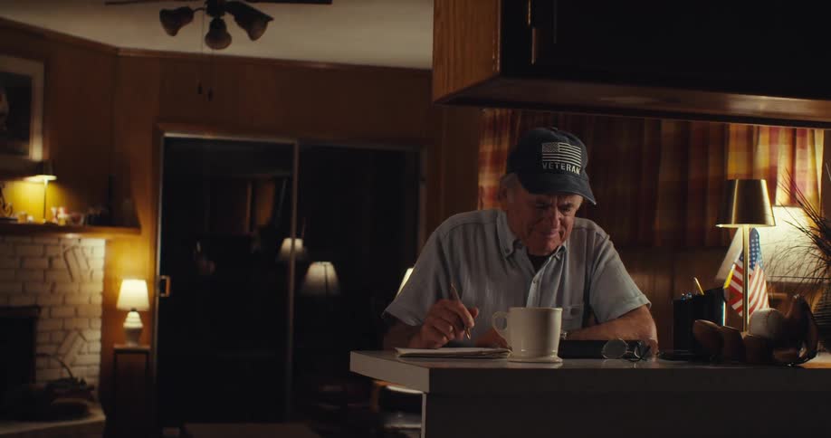 An old man has a cup of coffee in front of him as he writes with a pen