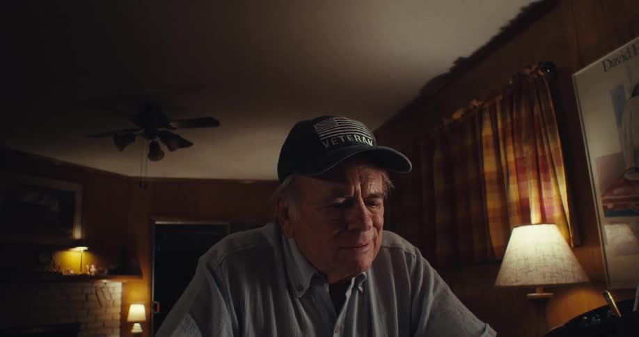 An elderly man is wearing a cap and glasses and then takes off his glasses and starts laughing