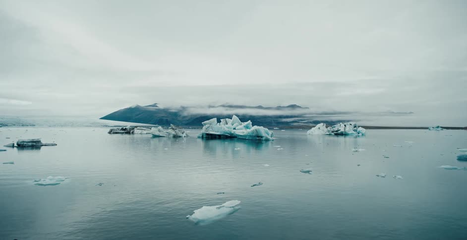 Melting icebergs and ice float across the arctic water under a cloudy sky