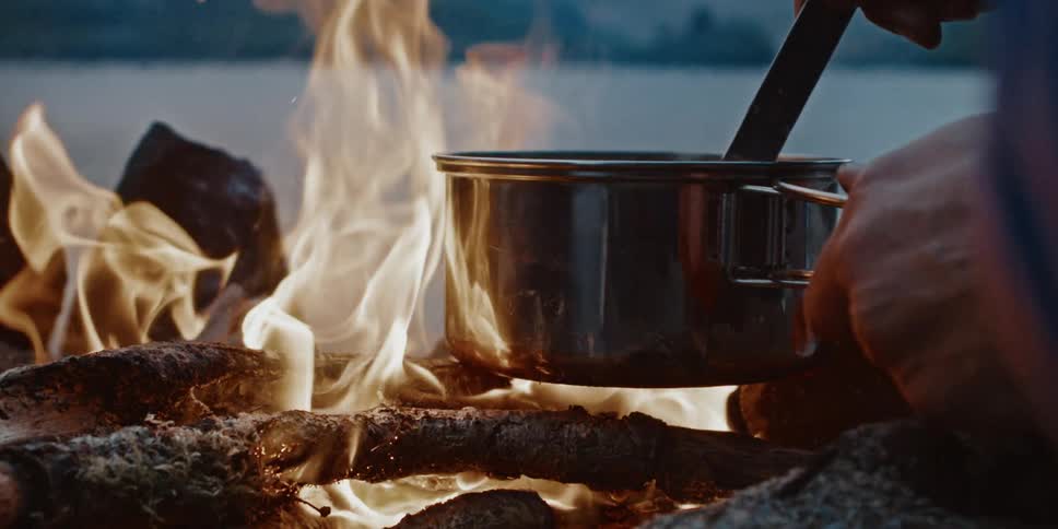 A footage of a person cooking out door in a stainless pot