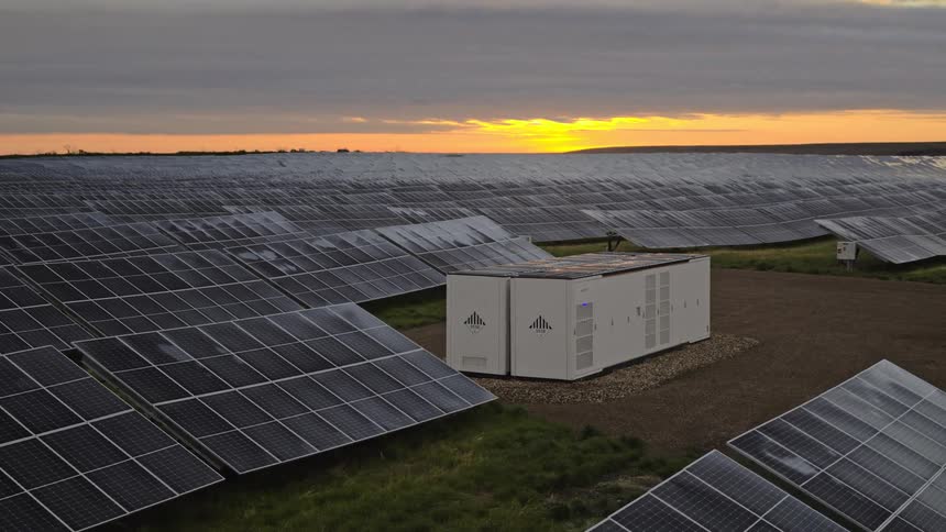 Field of solar panels at dawn with battery storage on site