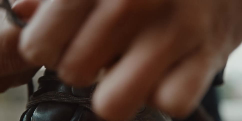 Hand adjusts the laces of a brown leather boot with focus on the stitching and eyelet details