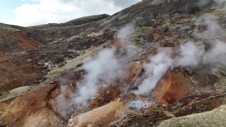Steam rises from geothermal vents in a hilly brown and green landscape