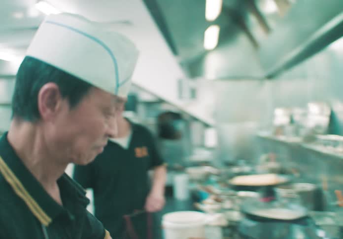 Two chefs of asian origin inside a restaurant kitchen preparing a variety of meals