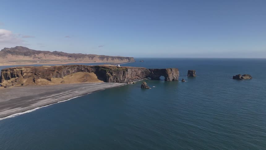 Dark cliffs jagged with stone arches stretch along the coast of iceland surrounded by deep blue sea and clear skies