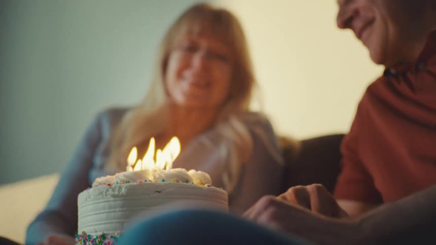 Older couple smiles at each other while the woman blows out the candles on her birthday cake