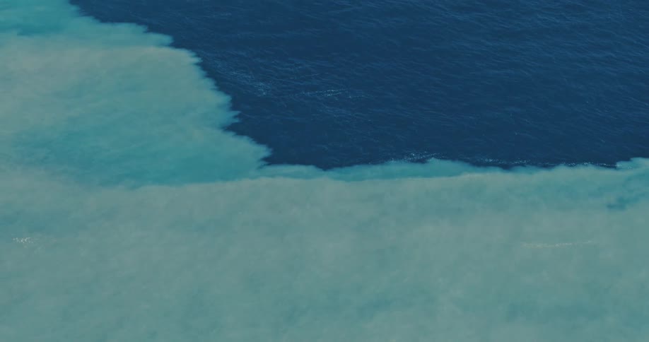 An aerial view shows a body of water where two areas of differing clarity meet with one section appearing as if ice is beneath the surface