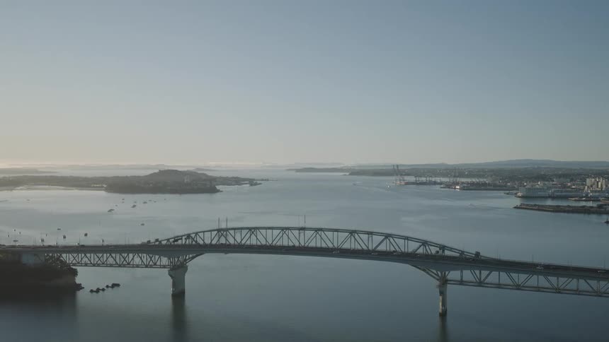 A large bridge crossing the sea with cars driving on it and a city with tall buildings in the background