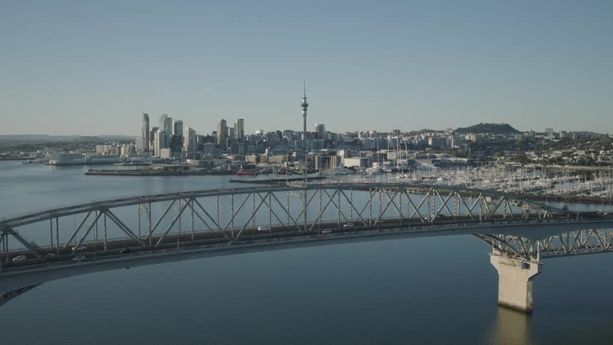 Aerial view of a large city skyline with a prominent bridge crossing over calm water in the foreground