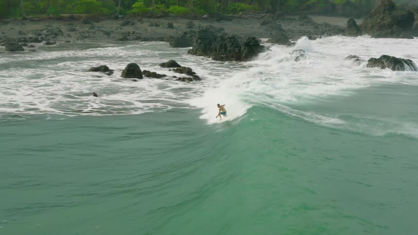 A person rides a wave as others sit on their surfboards waiting for more waves