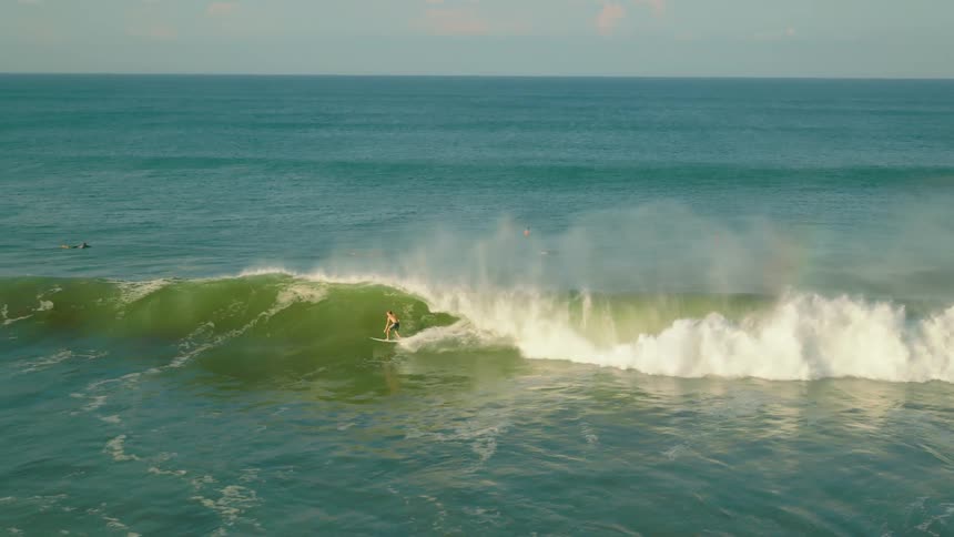 A man surfing a wave in the sea with other surfers sitting or lying on their boards in the background