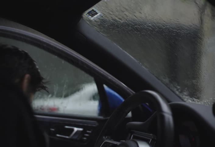 A man runs into the car from the rain outside