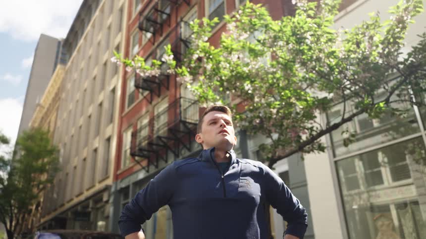 A man standing with his hands on his hips taking a deep breath on a street near residential buildings