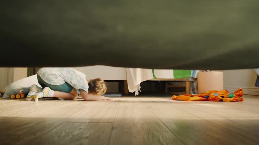 A child searches under the bed during a game of hide and seek