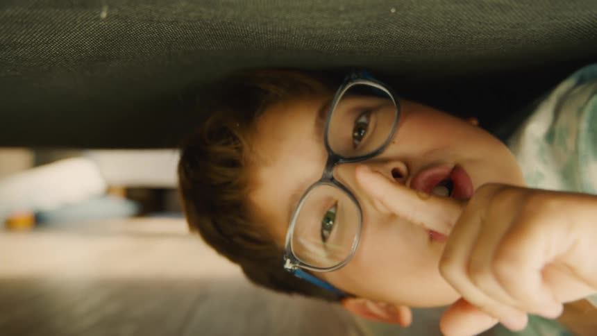A boy is playing hide and seek and crawls under the bed