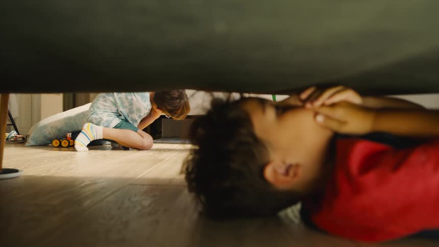 A child hiding under a bed while another child is looking for them