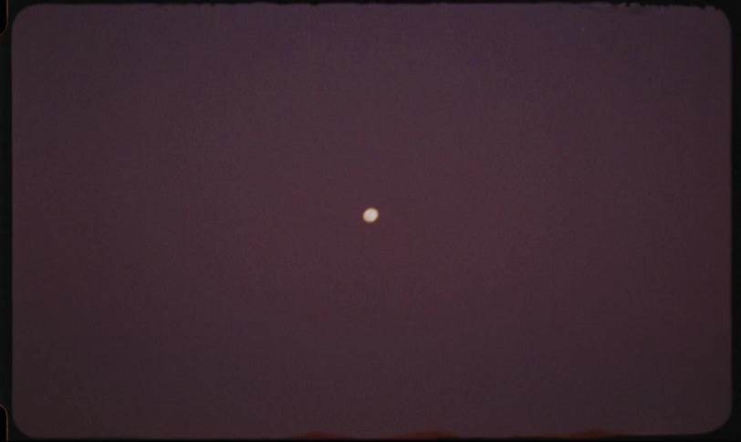 A woman in the desert wearing a hijab near a car with a full moon in the sky