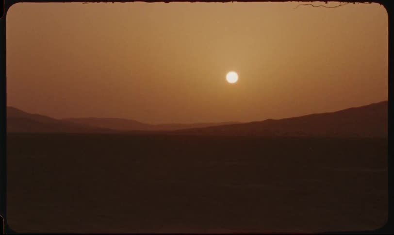 Closeup of a persons hand driving and a desert landscape appearing in the late afternoon