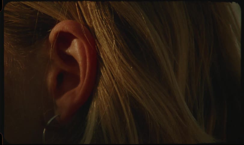 Closeup of a womans ear with blonde hair illuminated by warm light