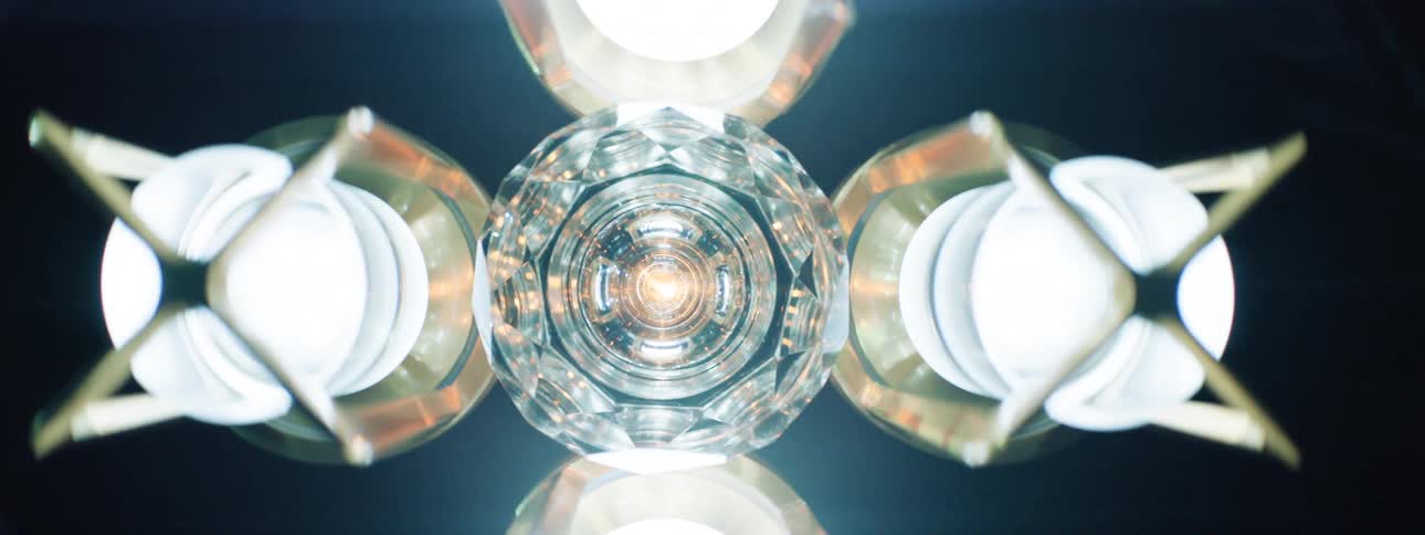 A lowangle shot captures a cluster illuminated ornate ceiling lights with a central multifaceted crystal surrounded by four round lights encased in metallic fixtures with angular designs against a dark ceiling