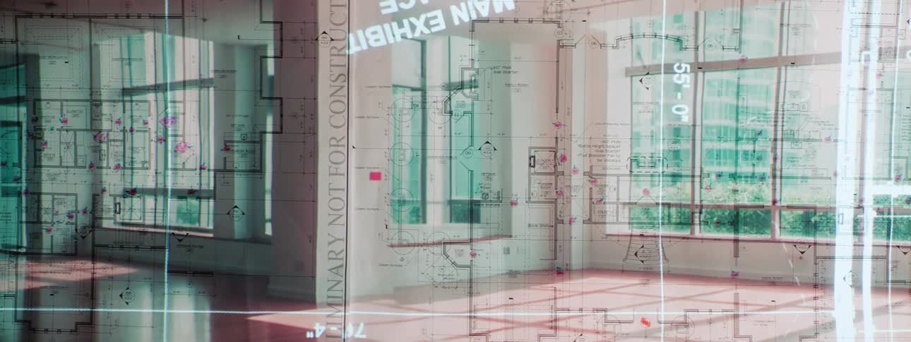 Architectural blueprints are overlaid on a view of a modern interior space with large windows reflecting an exterior scene